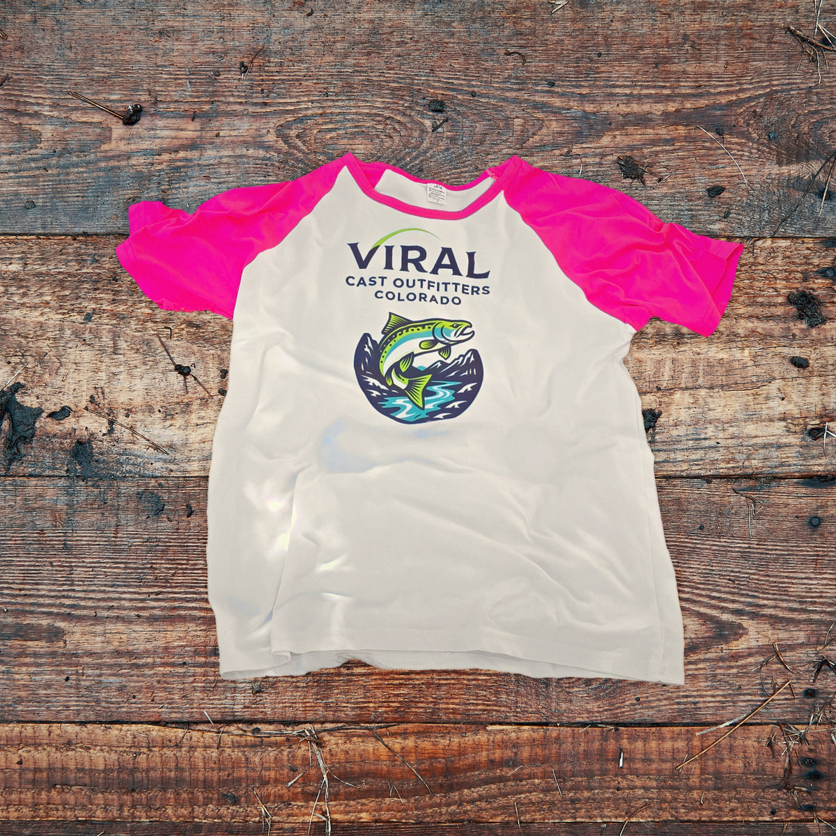 Viral Cast Outfitters white ringer shirt with pink sleeves and trout logo, laid flat on dark barn wood